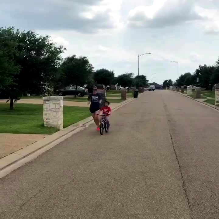 Video thumbnail showing: A woman runs next to her young son as he rides a bicycle without training wheels for the first time.  He heads toward a basketball pole and they both fall down as she tries to stop him.